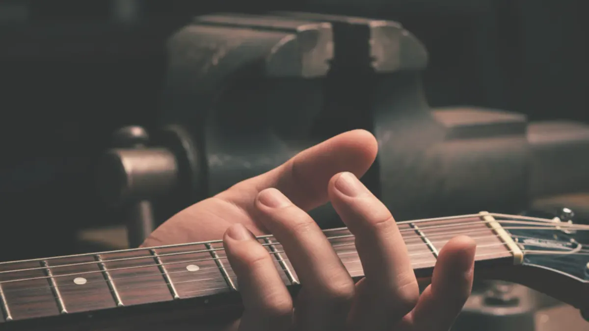 a hand tightly gripping guitar neck, in the background a vice representing the force of the grip 