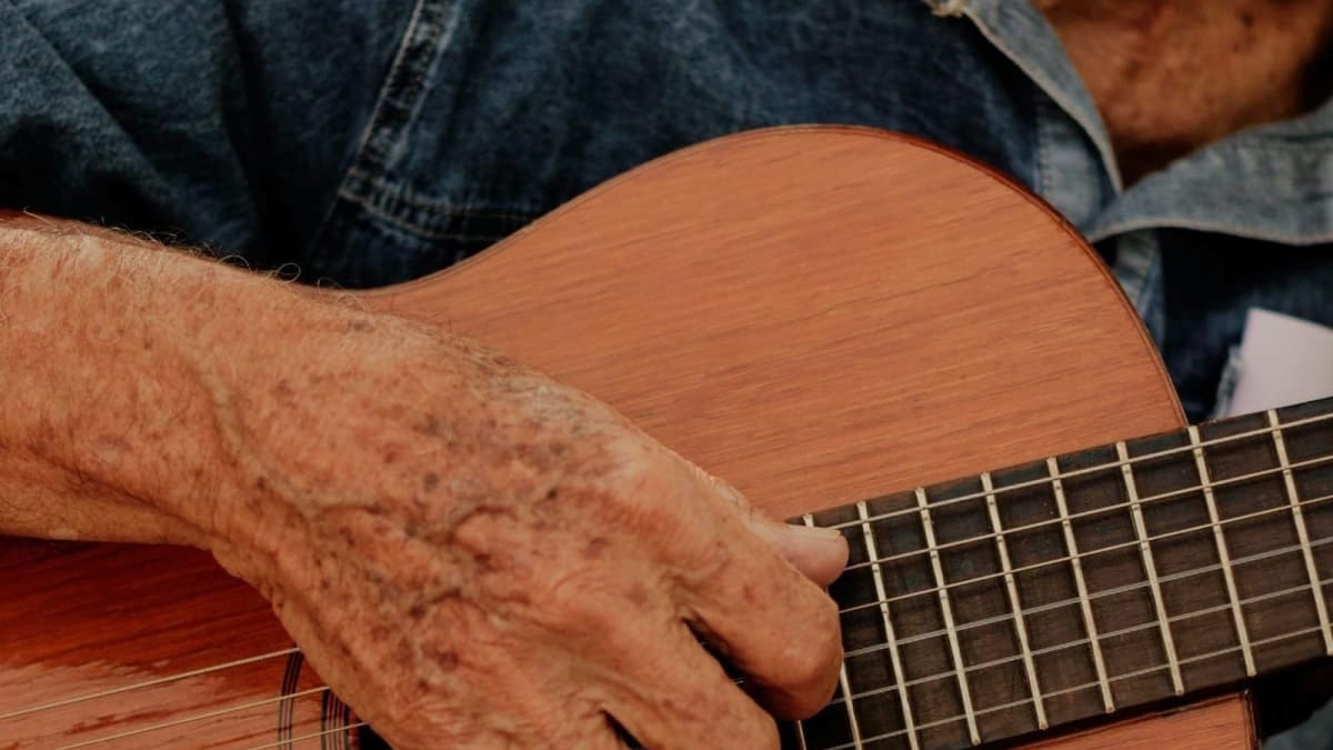 Middle-aged man playing guitar indoors, relaxed posture and focus