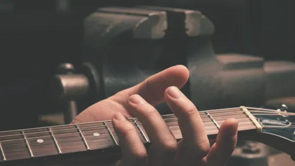 a hand tightly gripping guitar neck, in the background a vice representing the force of the grip 
