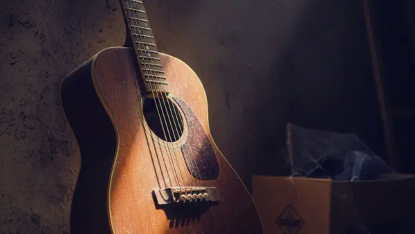 AN old dusty guitar sitting in the corner with sunlight shining on the strings inviting the user to play 