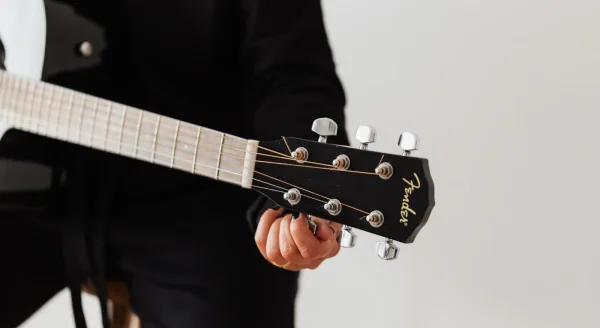 Guitarist retuning an acoustic guitar before trying an alternate tuning.